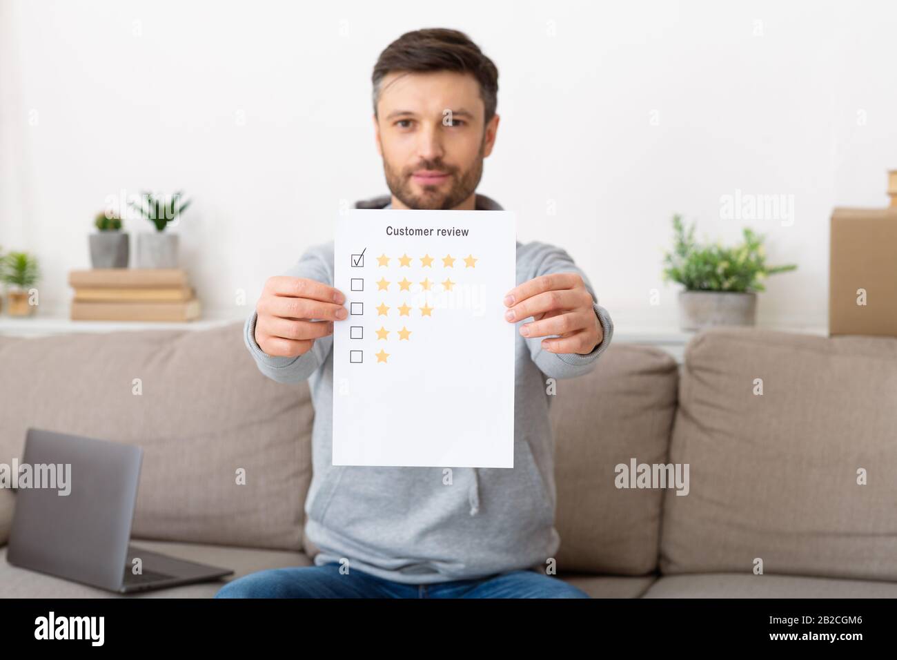 Buon giovane che tiene la revisione del cliente con la valutazione di cinque stelle Foto Stock