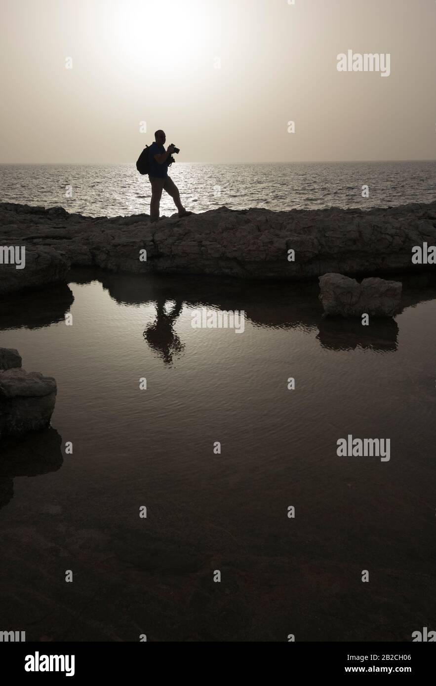 Silhouette fotografo contro il paesaggio marino. Ora del tramonto. Immagine monocromatica. Foto Stock