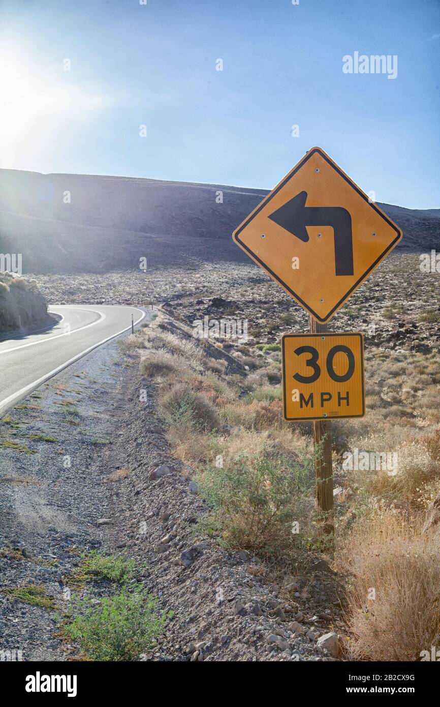 Il cartello giallo indica una svolta a sinistra e indica un limite di velocità di trenta miglia all'ora su una strada tortuosa attraverso il Parco Nazionale Della Valle Della Morte Foto Stock