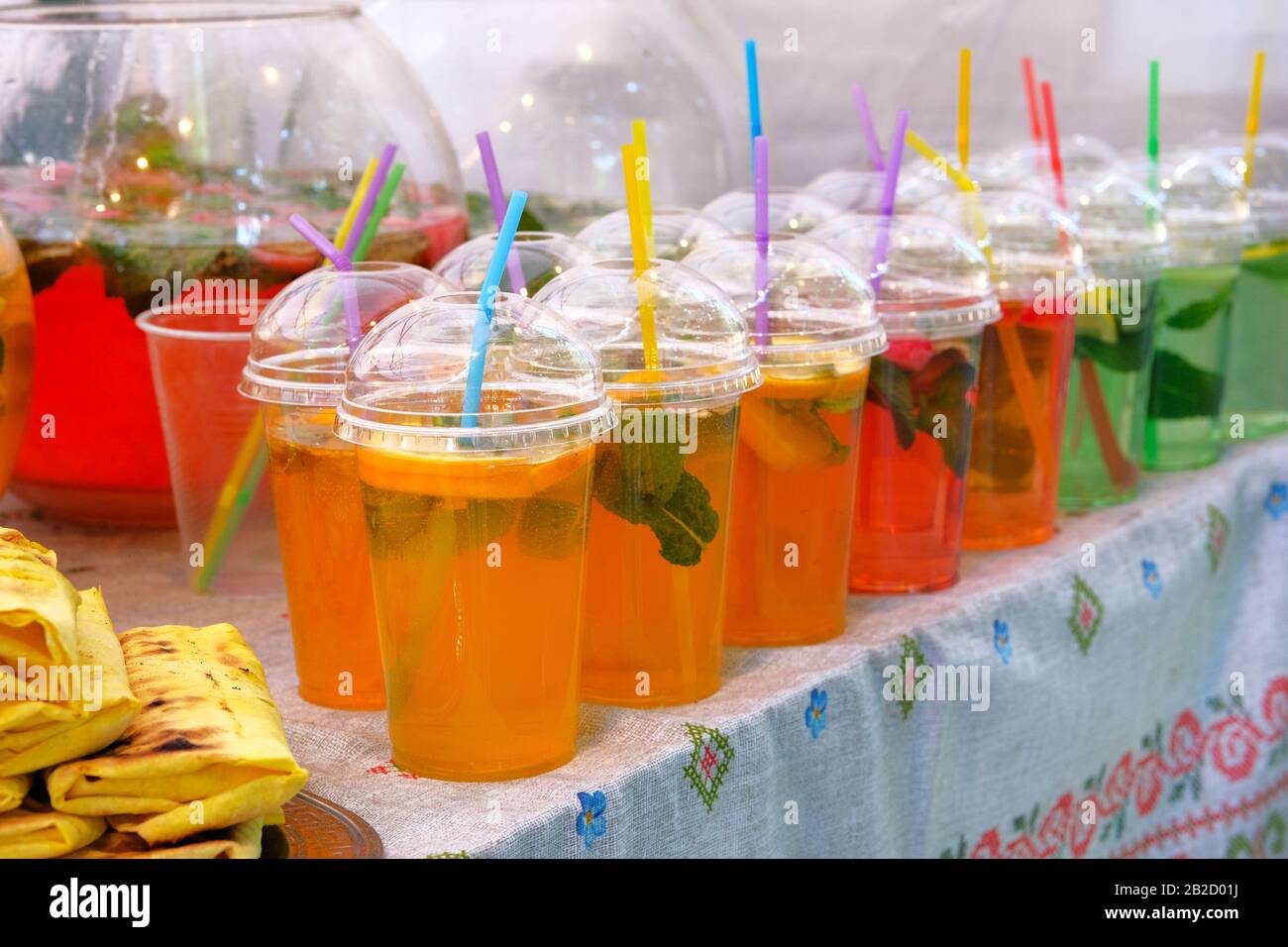 Bevande estive luminose con fette di limone, menta e acqua frizzante in tazza di plastica con paglia. Street food e cucina all'aperto. Foto Stock