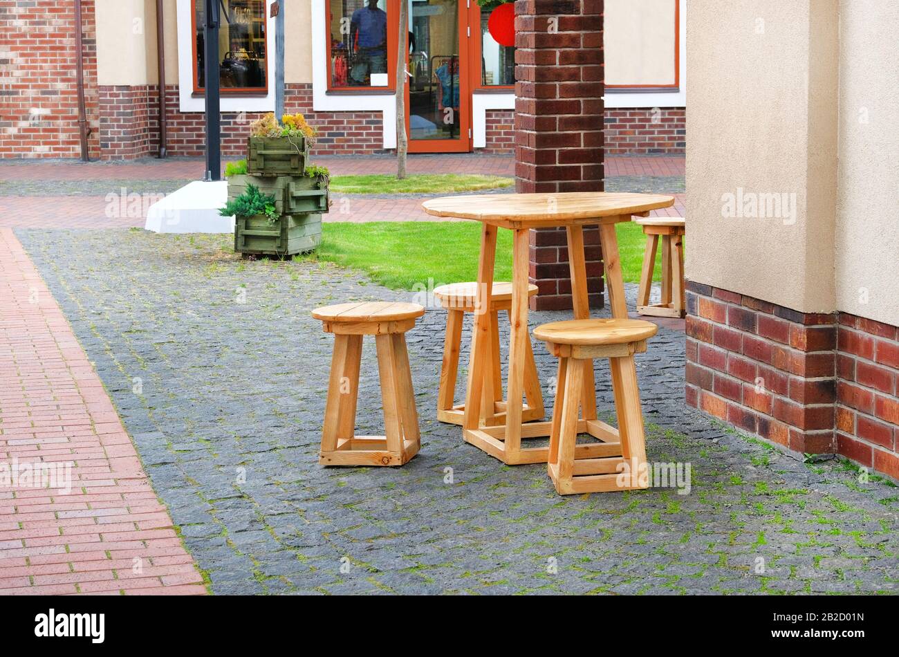 Caffè estivo. Tavolo e sedie in legno si trovano sul marciapiede in ciottoli vicino alle finestre del negozio. Design urbano Foto Stock