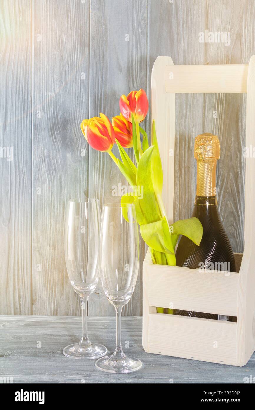 Una bottiglia di champagne in una scatola di legno. Accanto a 2 bicchieri di champagne e fiori di tulipano. La vacanza è l'8 marzo, festa della mamma. Ambiente romantico Foto Stock