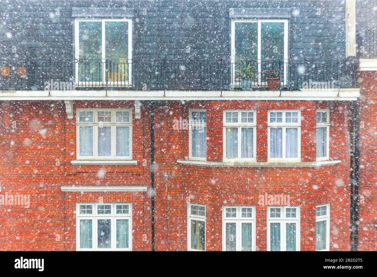 Neve pesante che cade a Londra con un palazzo in mattoni rossi sullo sfondo Foto Stock