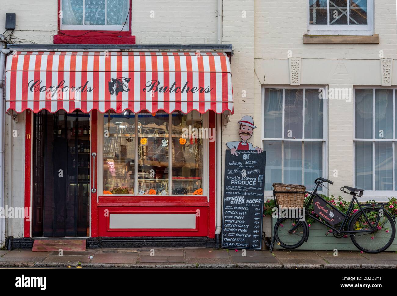 Un negozio di macellai tradizionale ad aylsham, Norfolk con tettoia a righe e bicicletta per la consegna vecchio stile appoggiata alla parete esterna. Foto Stock