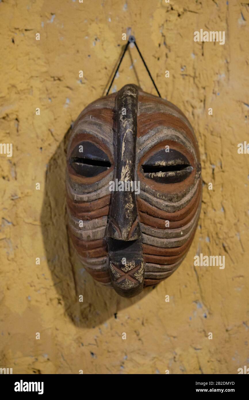 Maschera africana in legno appesa su un muro di pietra gialla. Foto Stock