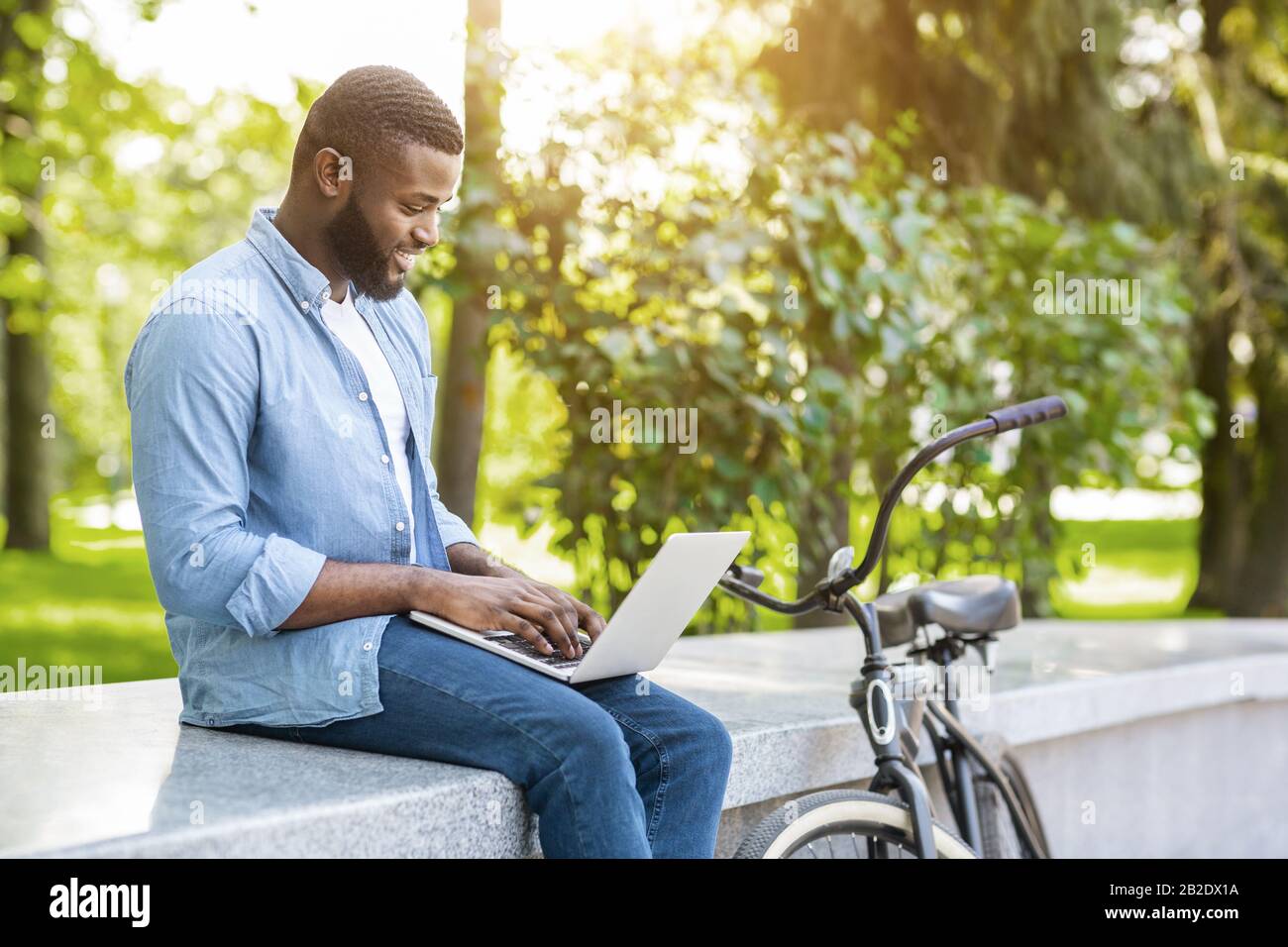 Wifi Spot Gratuito. Young Black Man Che Lavora Su Laptop A Park Foto Stock