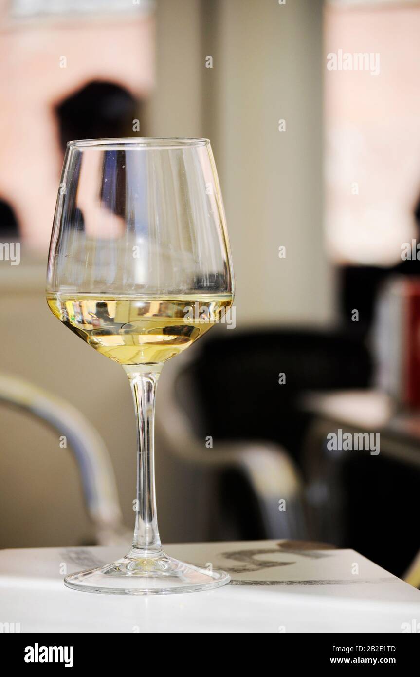 Primo piano di un bicchiere di vino bianco sul tavolo di un bar all'esterno. Sfondo fuori fuoco / bicchiere di vino su un tavolo Foto Stock