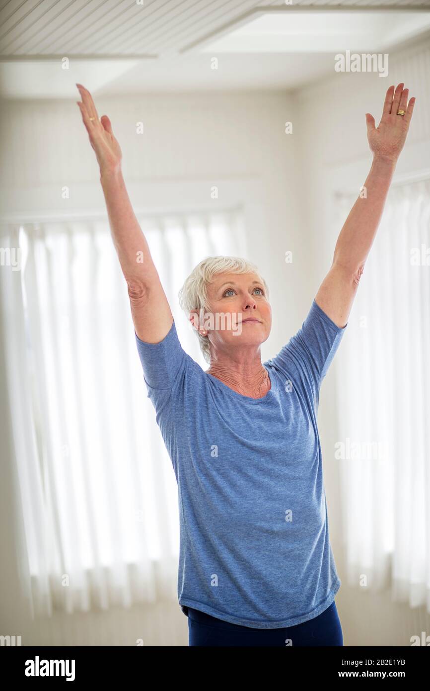Donna matura che allunga le braccia sopra la testa in una posa di yoga Foto Stock