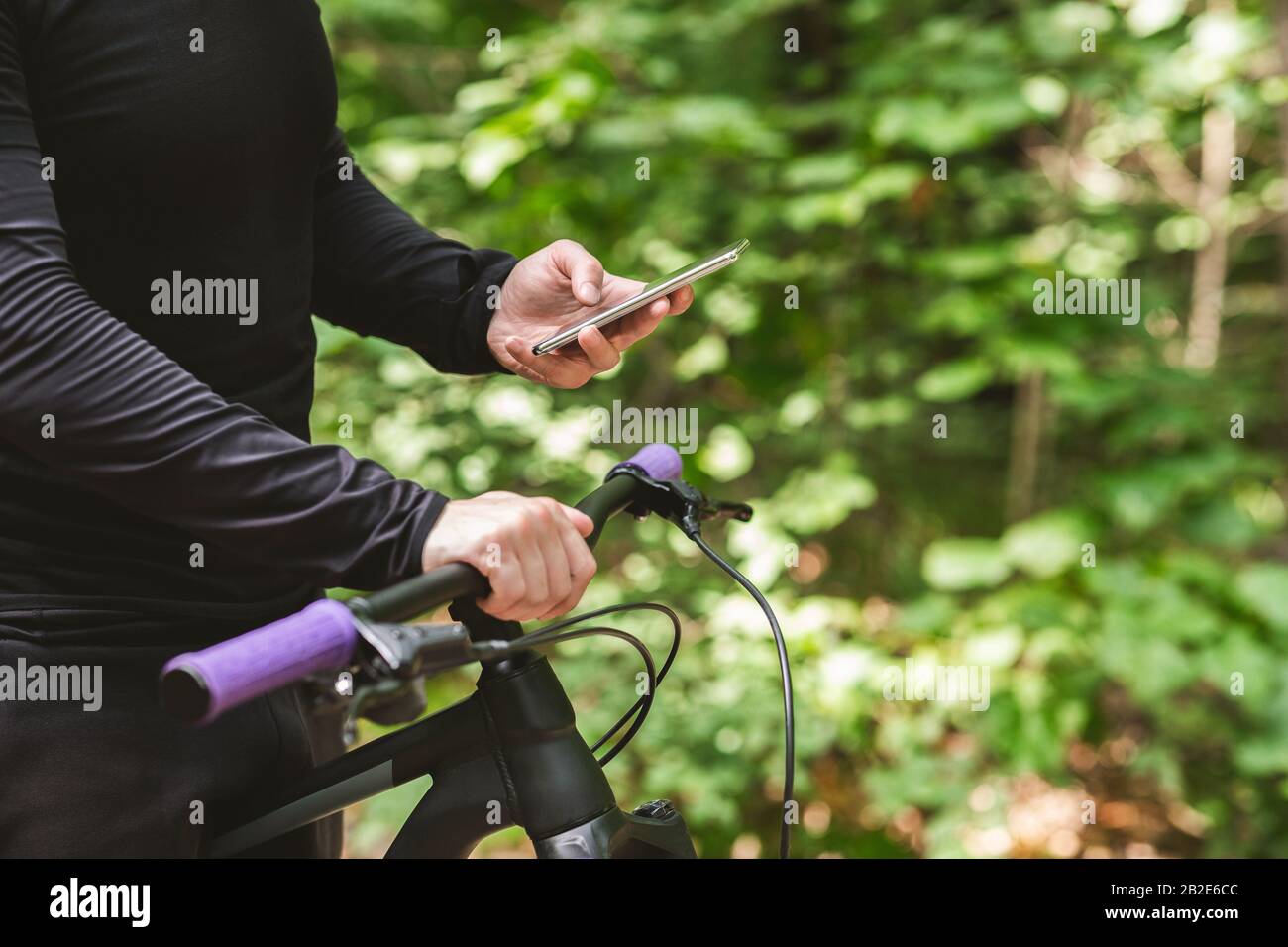 Primo piano del ciclista che tiene la bicicletta, utilizzando il telefono Foto Stock