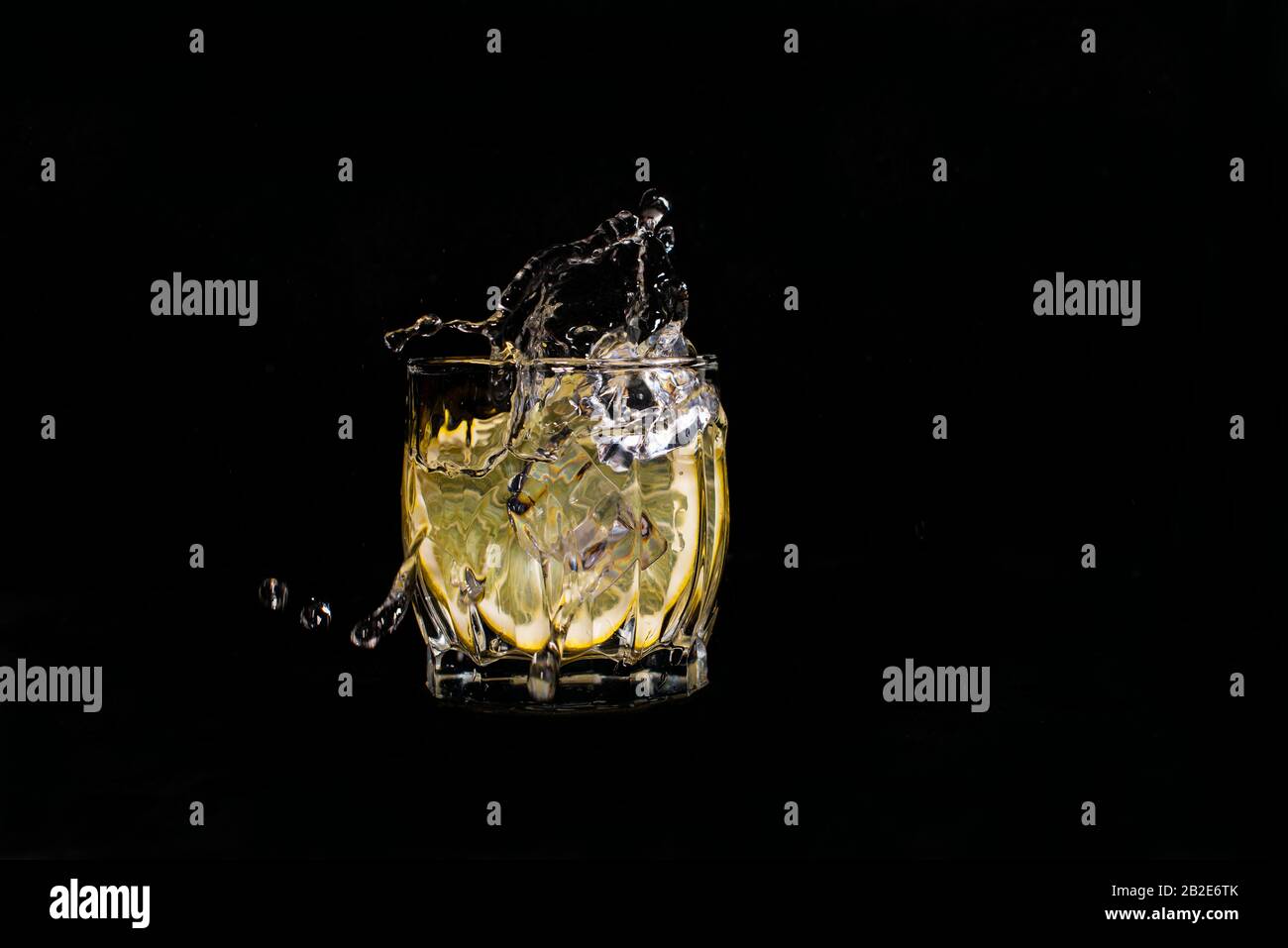 acqua aqua con soda al limone sversamenti quando il ghiaccio è gettato con gocce su uno sfondo nero Foto Stock