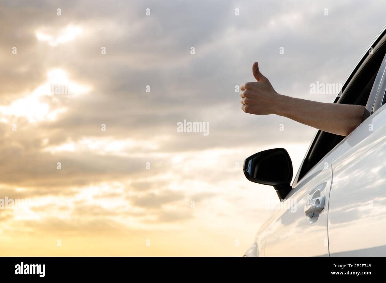 Uomo che mostra pollici in su / fare Come / Ok segno con la mano dalla finestra dell'auto con cielo tramonto, rilassante, godendo viaggio su strada e sentire l'aria e la libertà. T Foto Stock