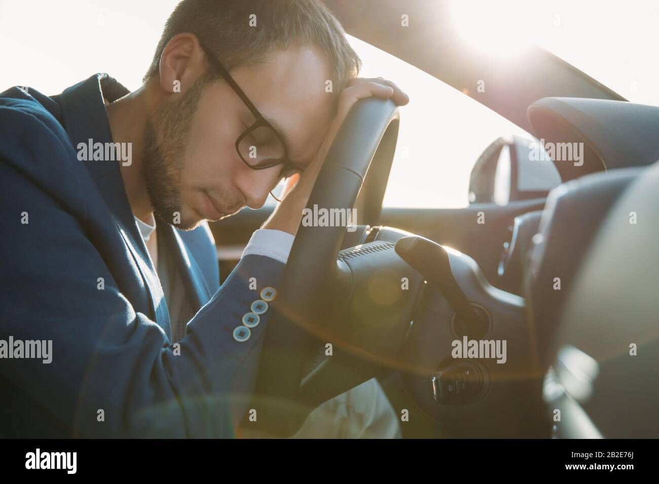 Un uomo d'affari stanco che si addormenta seduto all'interno della sua auto visto attraverso il parabrezza, si è fermato a riposare dopo la guida. Esausto, sonnolenza, affaticamento, overw Foto Stock