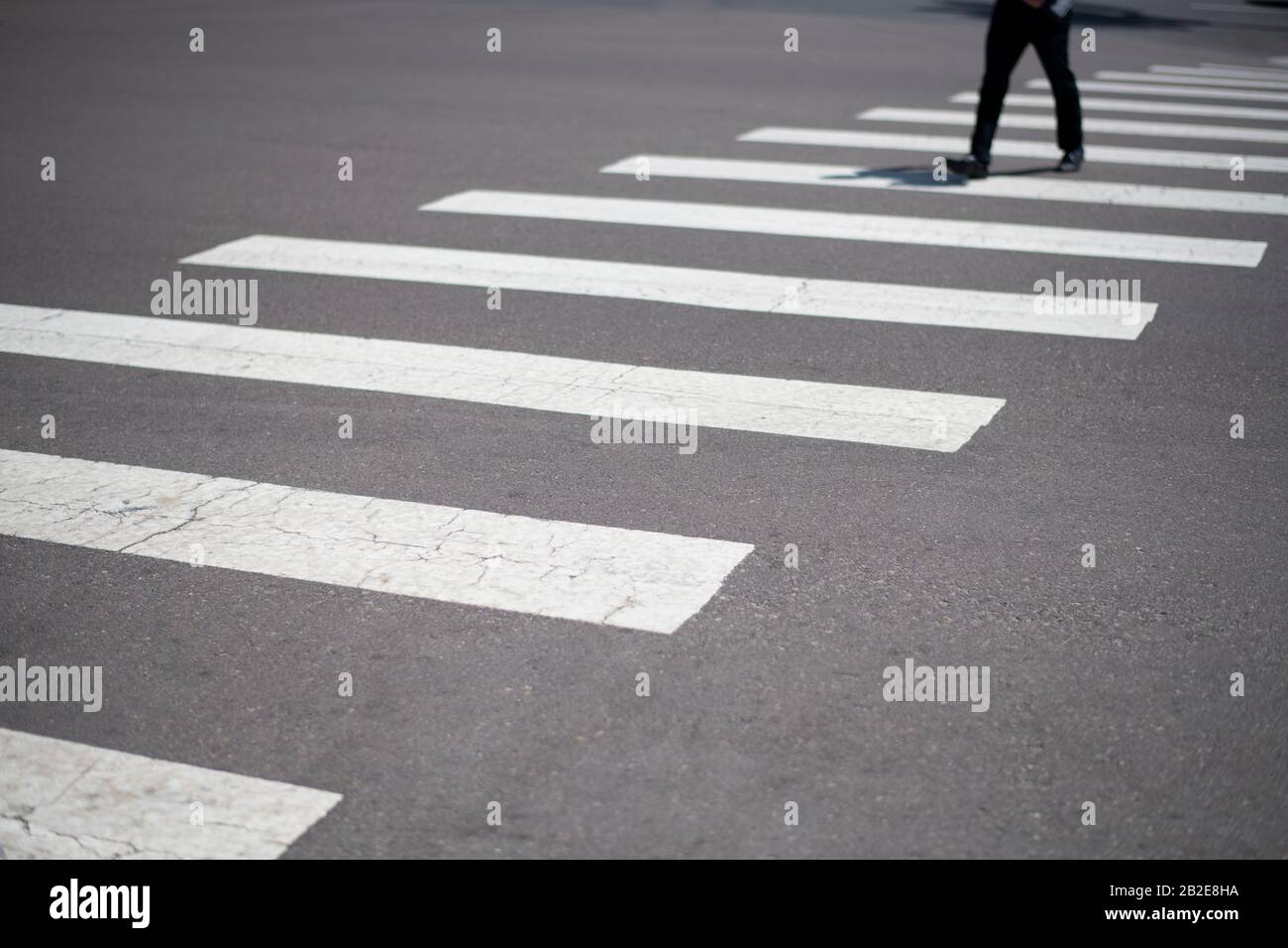 uomo d'affari che attraversa la strada urbana con le linee grafiche del crosswalk in primo piano Foto Stock
