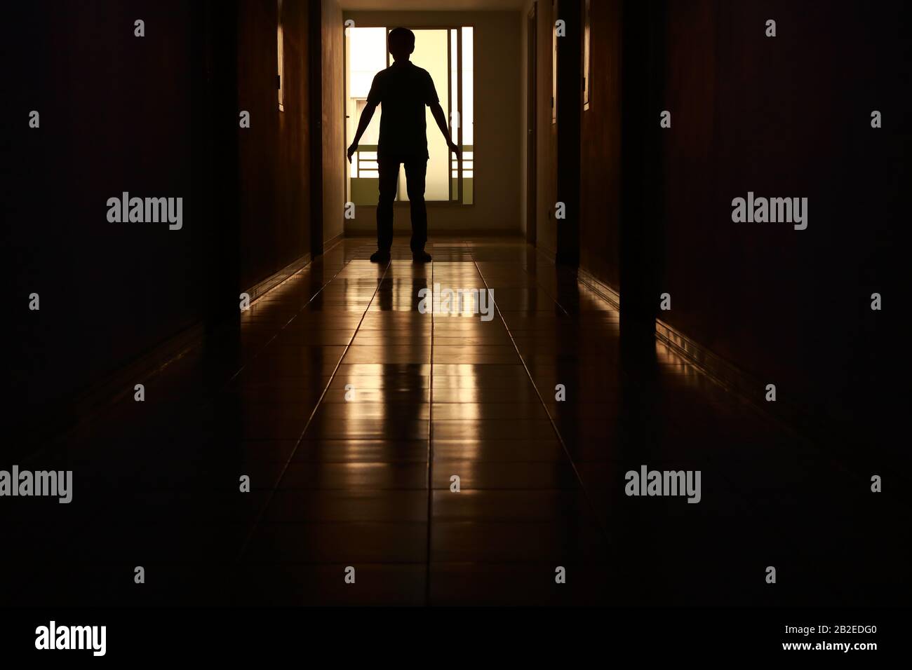 Silhouette di una persona misteriosa in piedi vicino alla fine del corridoio vuoto di un edificio Foto Stock