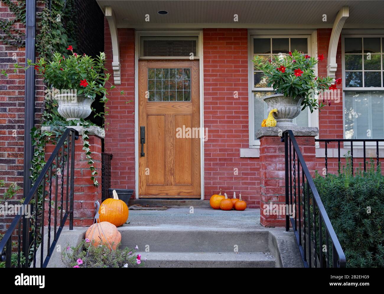 Portico anteriore di vecchia casa di mattoni con zucche e vasi di fiori Foto Stock