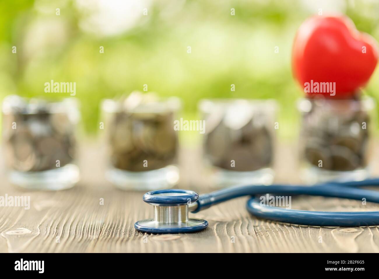 Primo piano stetoscopio blu e vaso di moneta su tavolo di legno. Concetto di controllo finanziario e monetario Foto Stock