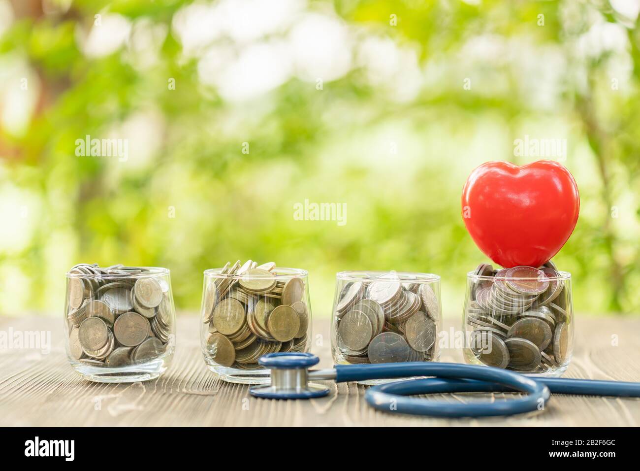 Primo piano stetoscopio blu e vaso di moneta su tavolo di legno. Concetto di controllo finanziario e monetario Foto Stock