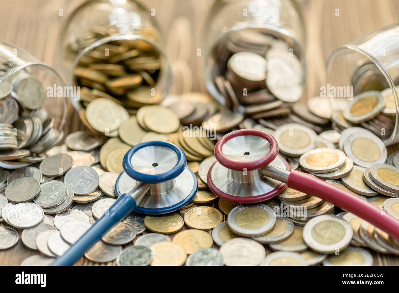 Primo piano stetoscopio blu e vaso di moneta su tavolo di legno. Concetto di controllo finanziario e monetario Foto Stock