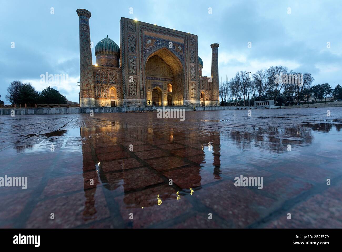 Sher Dor Madrasa con riflessione in Puddle in una fredda giornata di pioggia invernale, Registan, Samarcanda, Uzbekistan Foto Stock