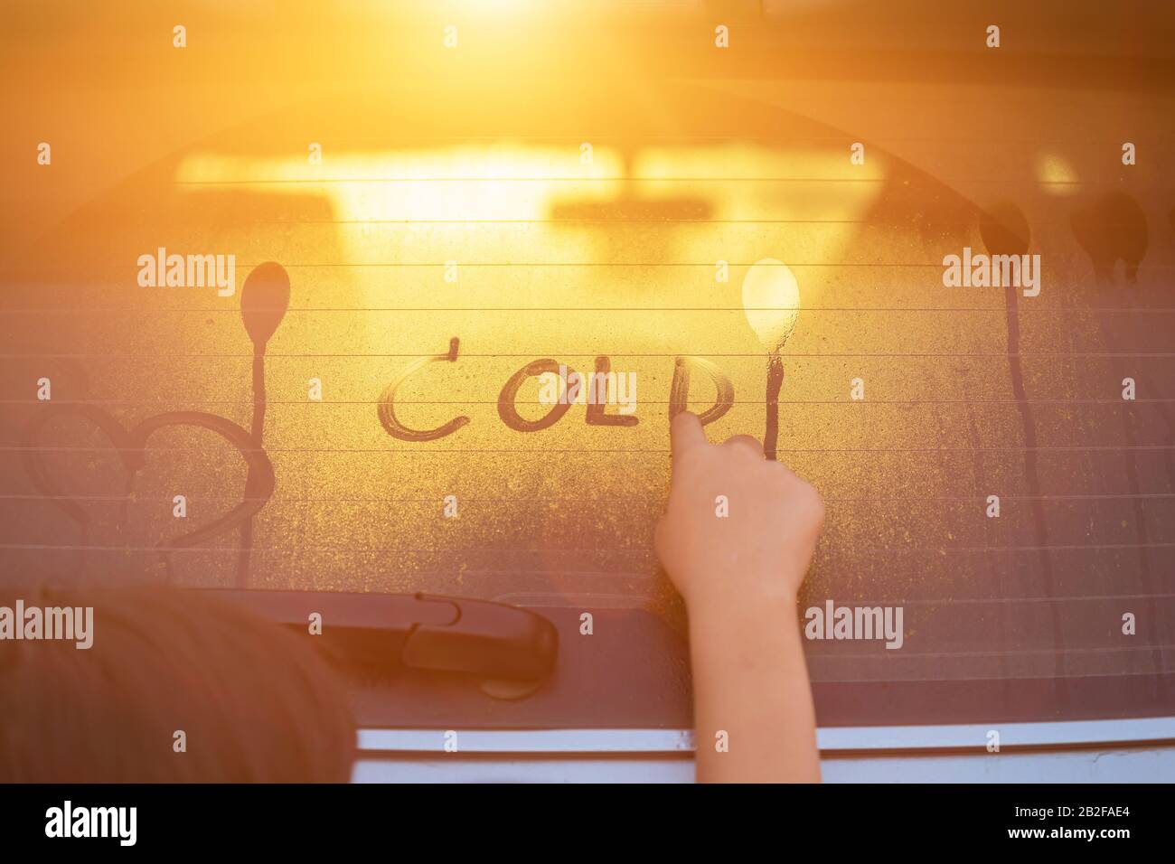 I bambini che scrivono la parola 'FREDDO' sullo specchio posteriore bagnato della sua automobile del SUV del padre nel tempo di mattina per il concetto di inverno Foto Stock