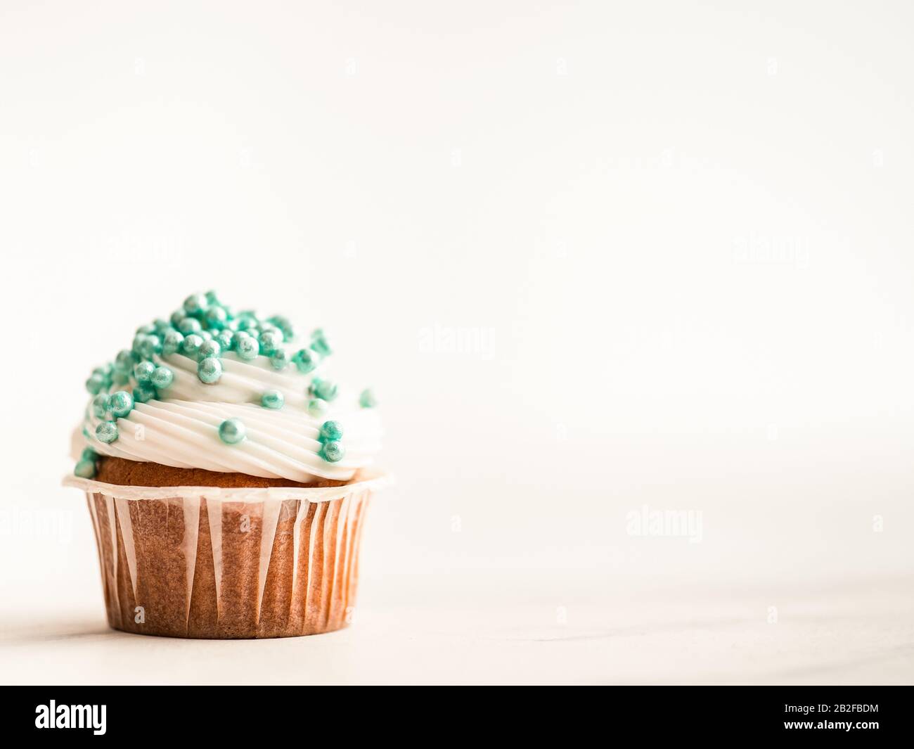 Cupcake decorato con spruzzette blu e copia spazio a destra. Sfondo in marmo bianco. Foto Stock