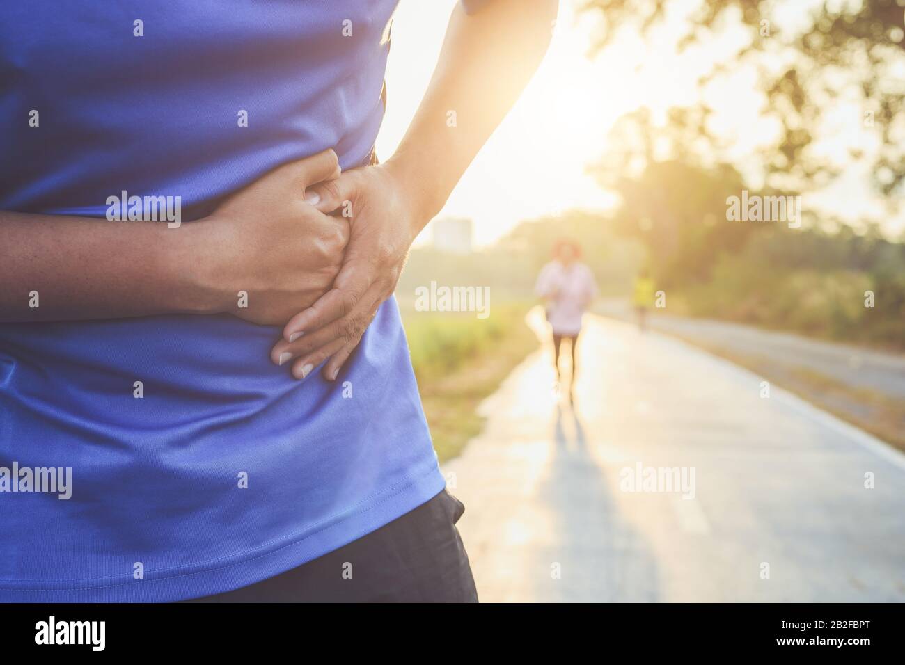 Crampi allo stomaco o lesioni mentre il concetto di allenamento : l'uomo asiatico di usare le mani tenere sul suo stomaco durante il funzionamento su strada nel parco Foto Stock
