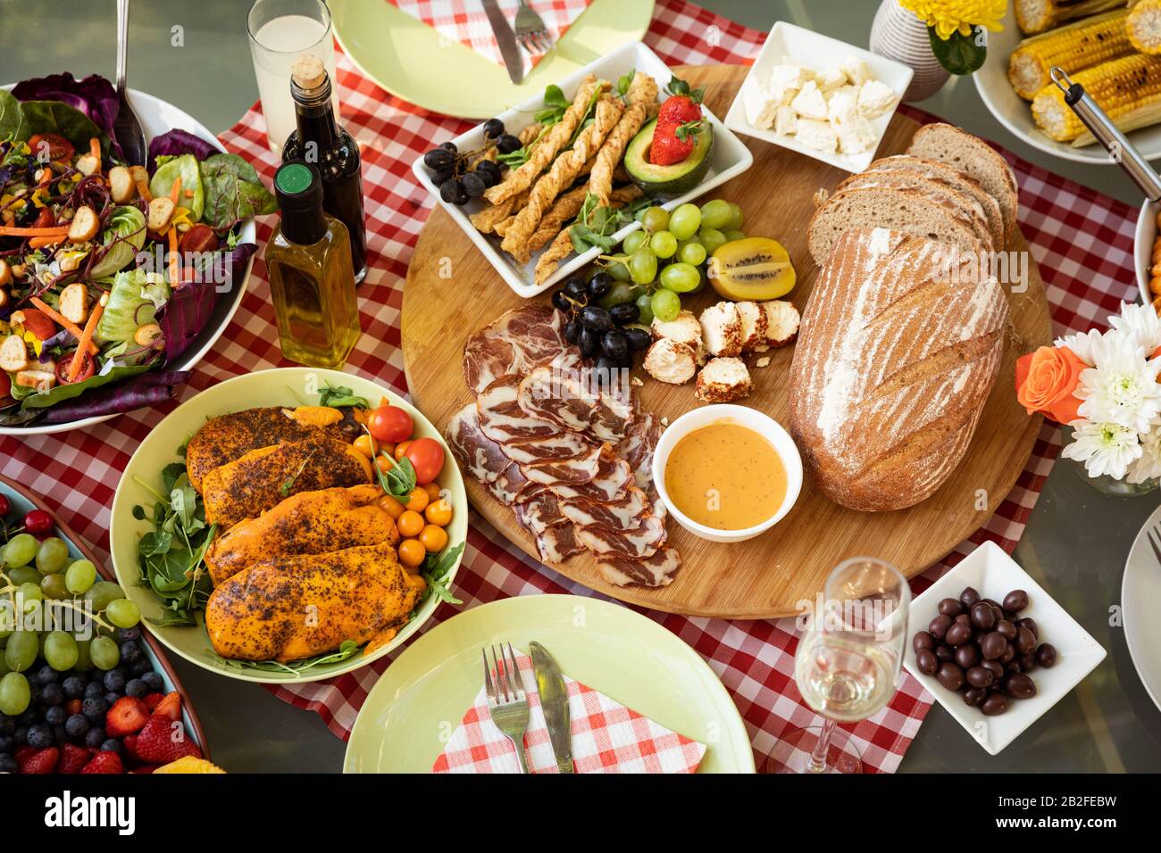 Vista dall'alto di una ciotola di insalata, pane, carni, frutta e altri alimenti, pronti a mangiare su un tavolo all'aperto con una tovaglia rossa di gingham, decorata con Foto Stock