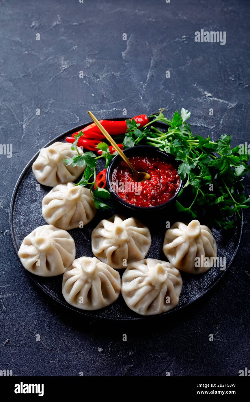 Khinkali, gnocchi con ripieno di carne servito su un piatto nero con jadika e coriandolo fresco, cucina georgiana, vista verticale dall'alto Foto Stock