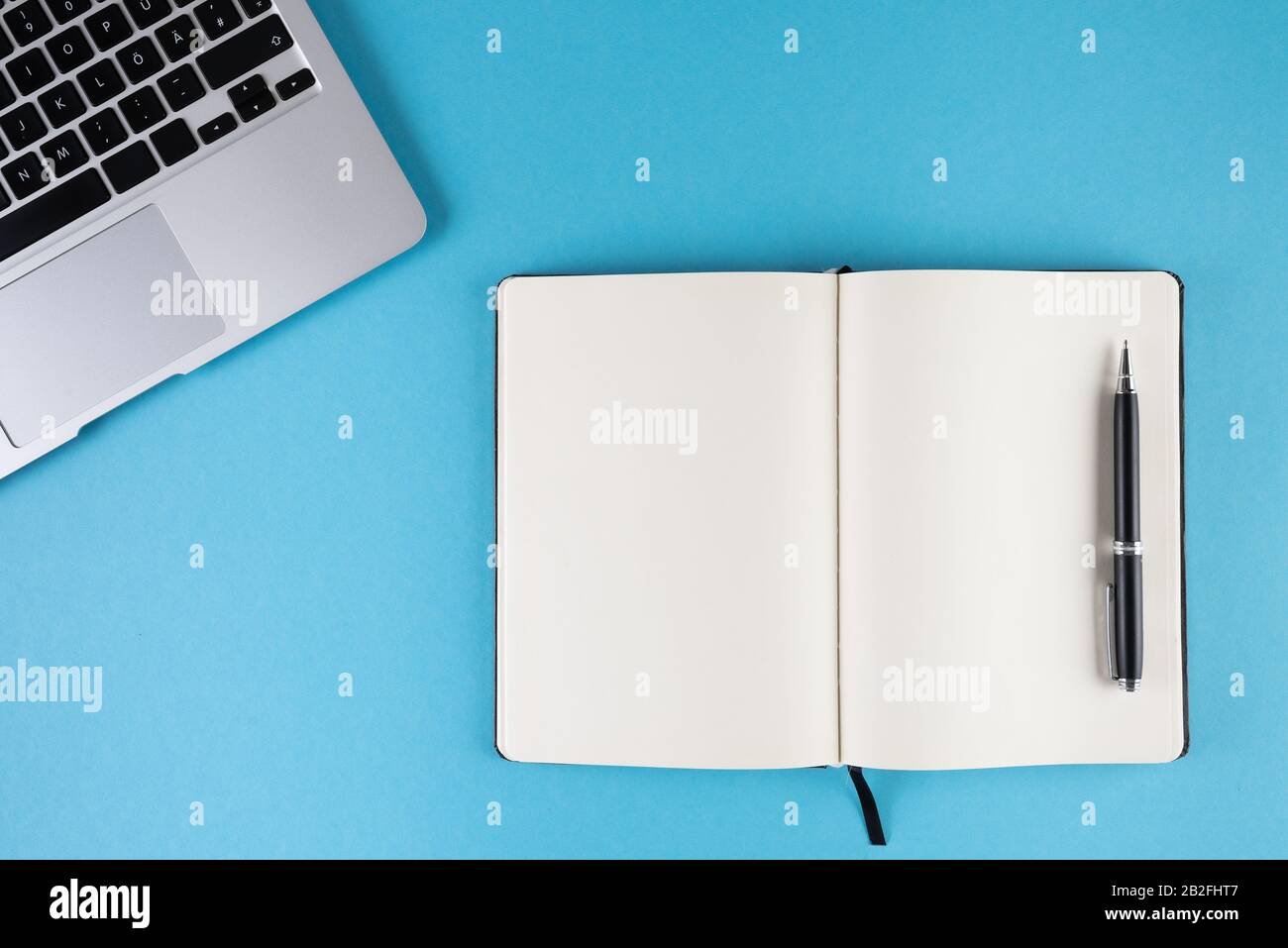 aprire un diario o un notebook con pagine bianche vuote e un computer portatile su un modello di sfondo blu Foto Stock