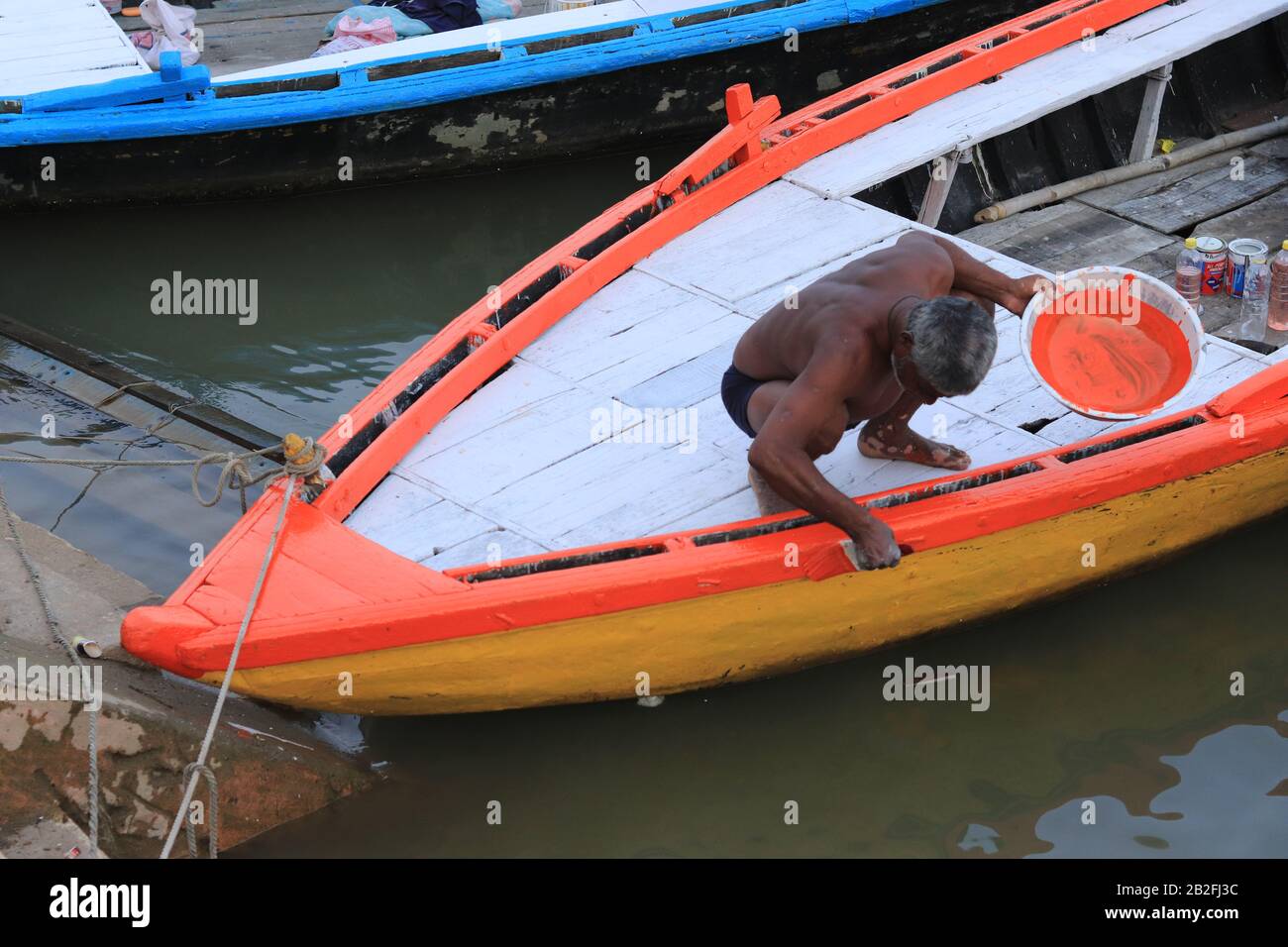 Un uomo indiano che dipinge la sua barca con colore arancione Foto Stock