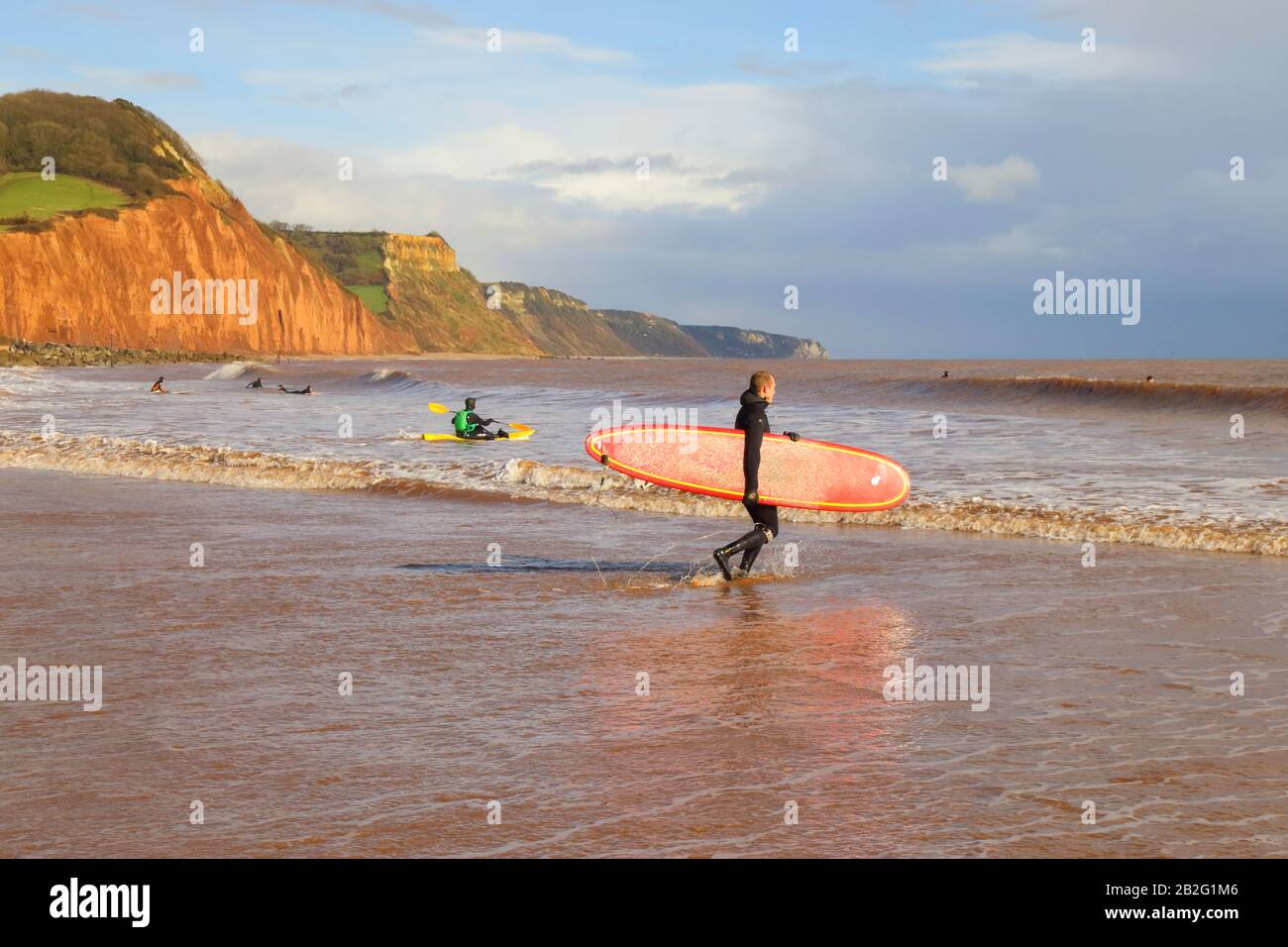 Surfista in muta che trasporta il surfboard sulla spiaggia a Sidmouth, Devon Foto Stock