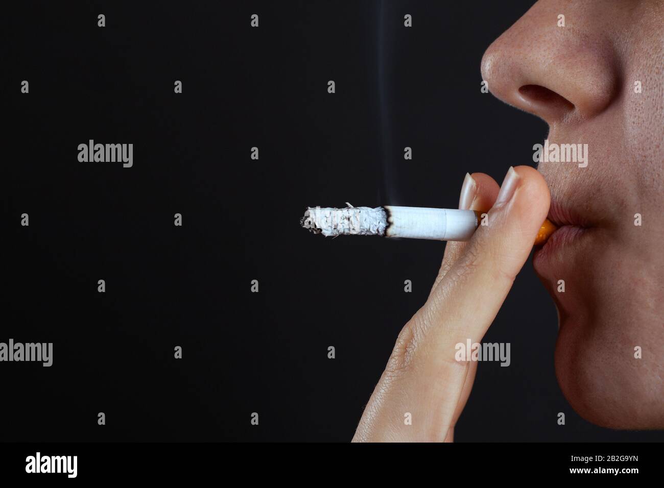 la donna fuma una sigaretta su sfondo scuro, la dipendenza dalla nicotina, il fumo un prodotto del tabacco. Foto Stock