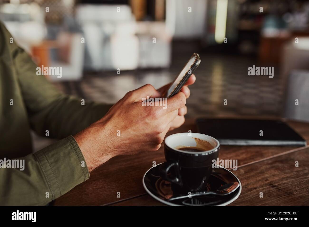 Chiudiere le mani dell'uomo usando lo smartphone mentre si siede nel caffè che beve il caffè Foto Stock