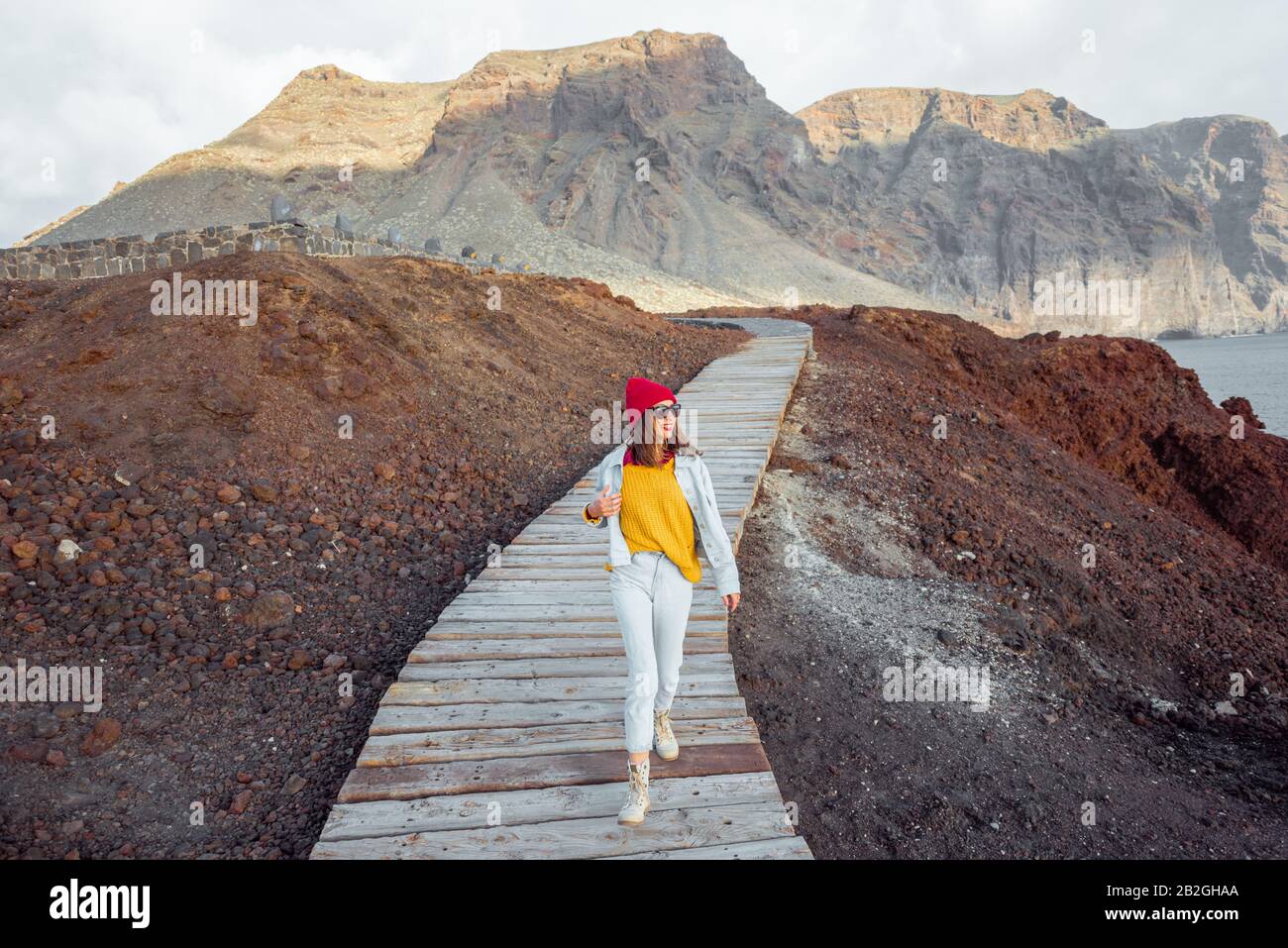 Donna che cammina sul pittoresco sentiero in legno attraverso la terra rocciosa con le montagne sullo sfondo. Viaggiando sul capo nord-ovest dell'isola di Tenerife, Spagna Foto Stock