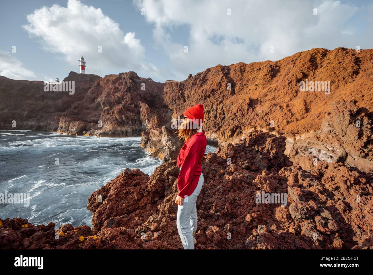 Donna che gode di una splendida vista sulla costa rocciosa dell'oceano e un faro sullo sfondo, viaggiando sul capo Teno a nord-ovest dell'isola di Tenerife, Spagna Foto Stock