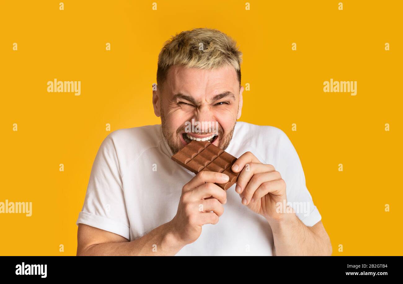 L'uomo dolce dente morde felicemente cioccolato isolato su sfondo giallo Foto Stock