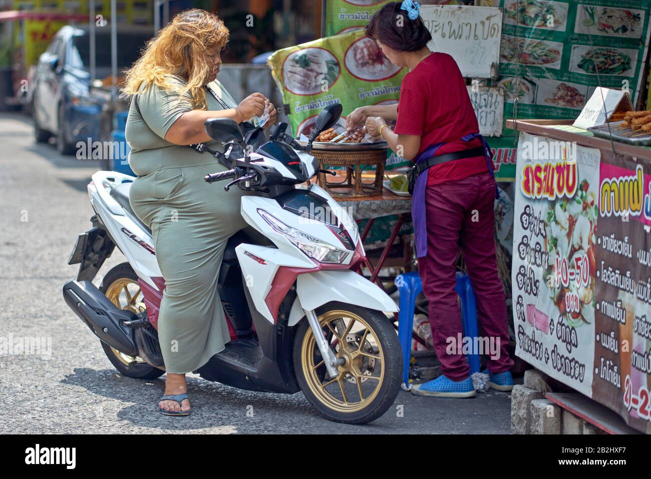 Donna obesa su una motocicletta che raccoglie cibo da una stalla di cibo di strada. Thailandia Sud-Est Asiatico Foto Stock