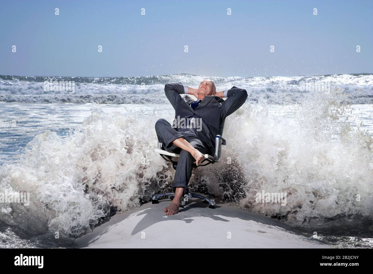 Uomo d'affari senior seduto su sedia da ufficio sulla spiaggia che è schizzato dalle onde Foto Stock
