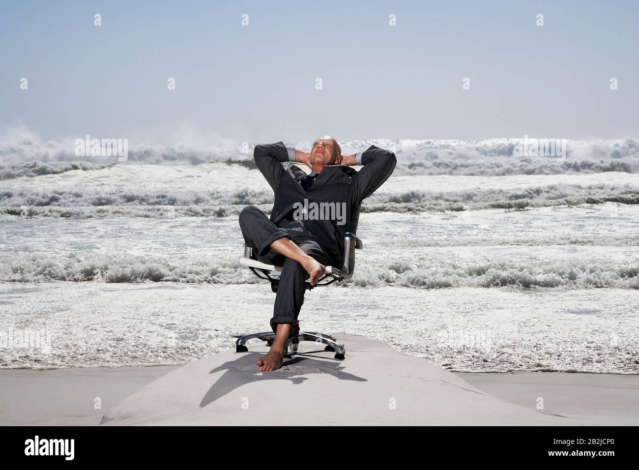 Uomo d'affari senior seduto su sedia da ufficio sulla spiaggia Foto Stock