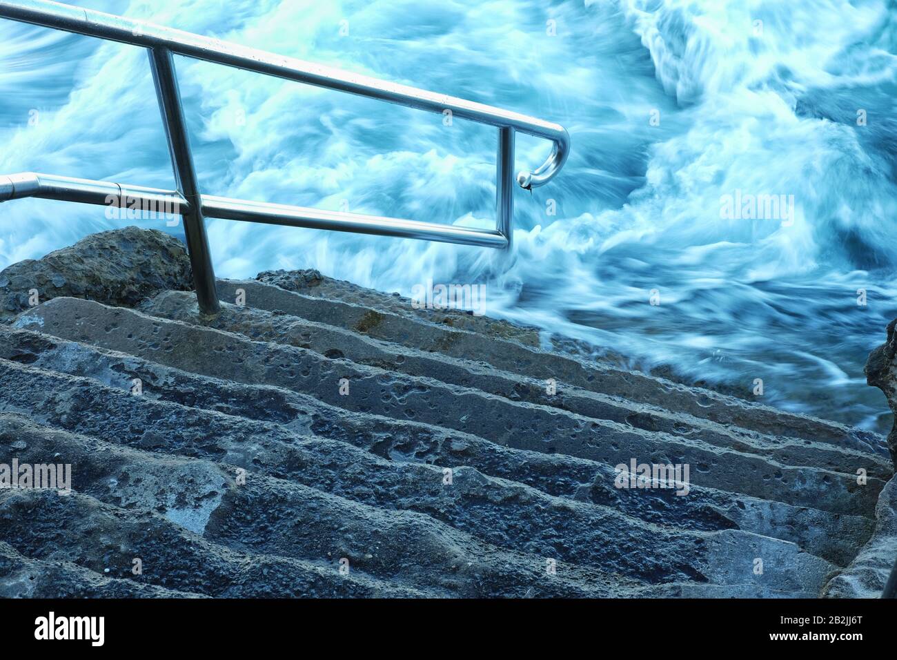 Ondulati acque bianche dell'oceano, schiume e lavaggi intorno ai gradini inferiori e corrimano Dei Bagni Giles, piscina di roccia oceanica Coogee Bay, Sydney, Australia Foto Stock