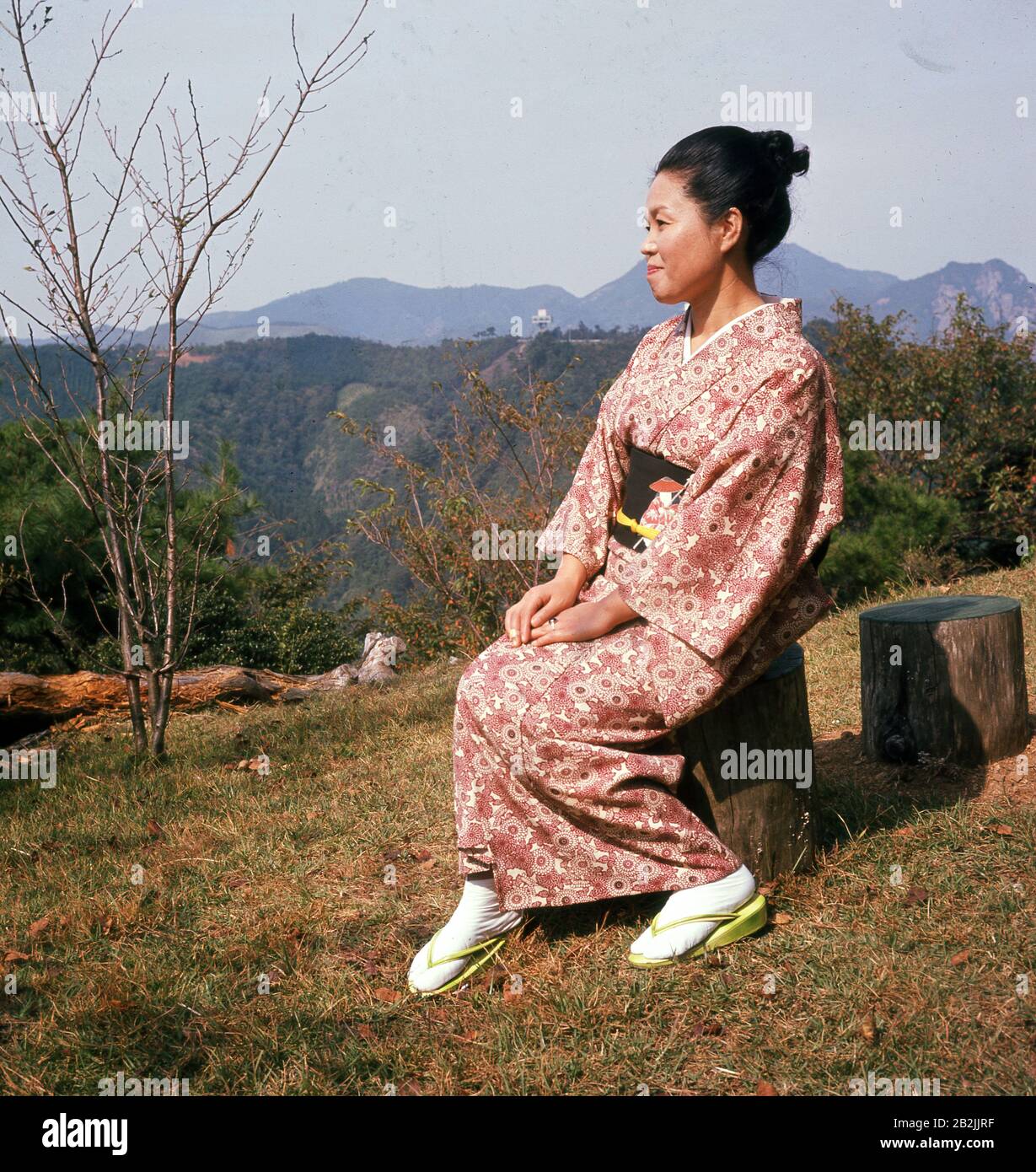 1960s, storico, una signora giapponese seduto su una collina che indossa il  costume tradizionale femminile, il kimono. Normalmente in seta, il vestito  ha maniche grandi e va dalle spalle ai talloni. Sono