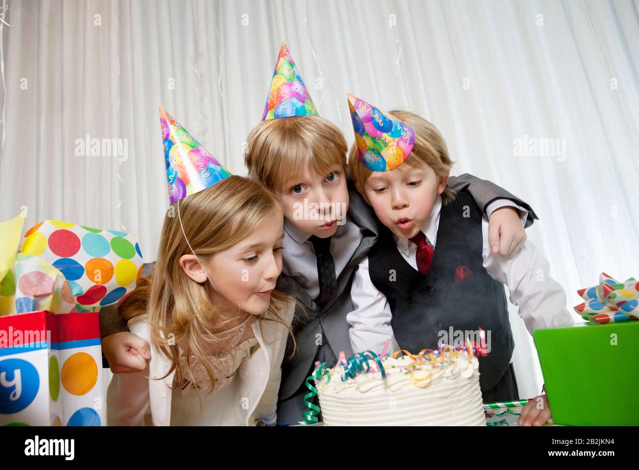 Fratelli e sorella che soffiano candele sulla torta di compleanno insieme Foto Stock