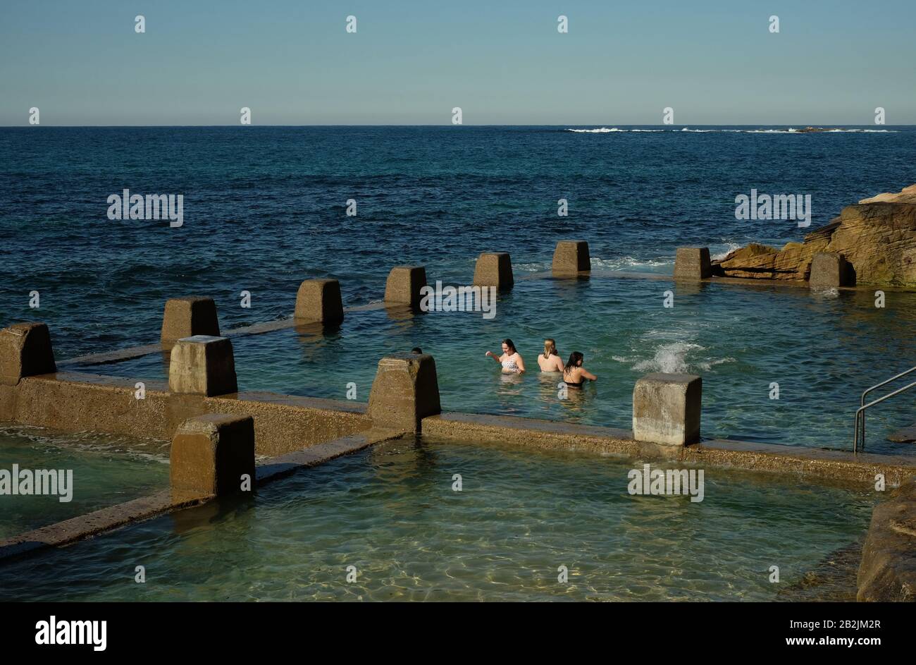 Tre giovani donne nel fresco blu-verde acqua di mare delle pareti piscina merlato, Ross Jones Rockpool, bordo dell'Oceano Pacifico del Sud, Sydney Foto Stock