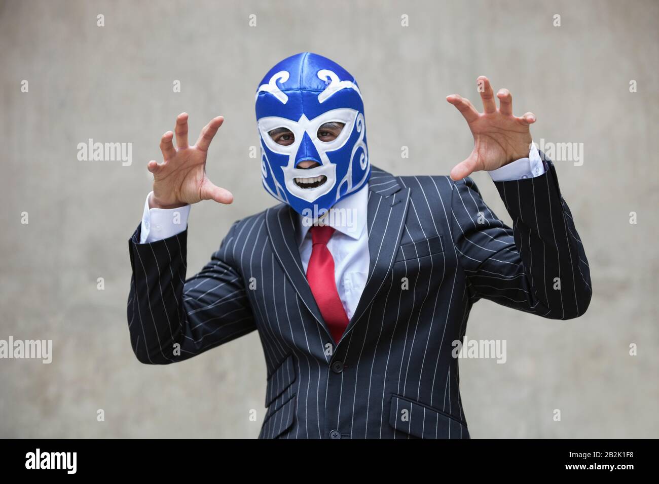 Giovane uomo d'affari che gesture nella maschera di wrestling e nei pinstripes si suit sopra lo sfondo grigio Foto Stock