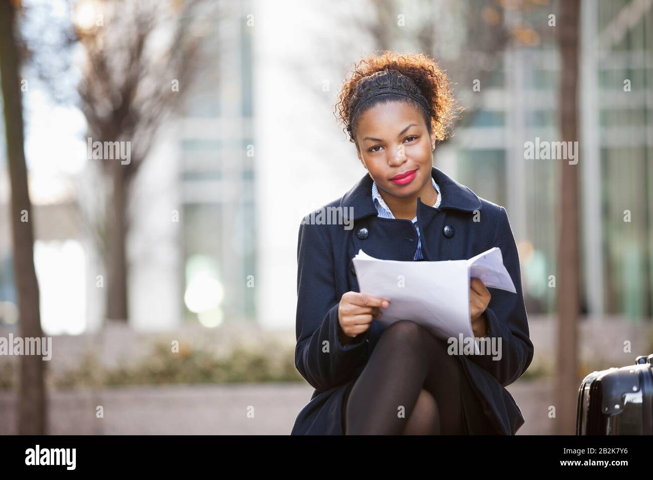 Ritratto di sicura giovane donna afroamericana con documenti seduti all'aperto Foto Stock