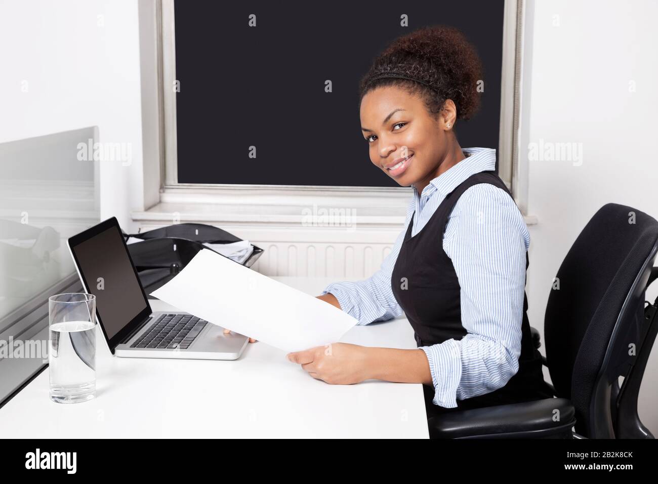 Ritratto di donna d'affari sorridente con documento che usa il laptop alla scrivania in ufficio Foto Stock