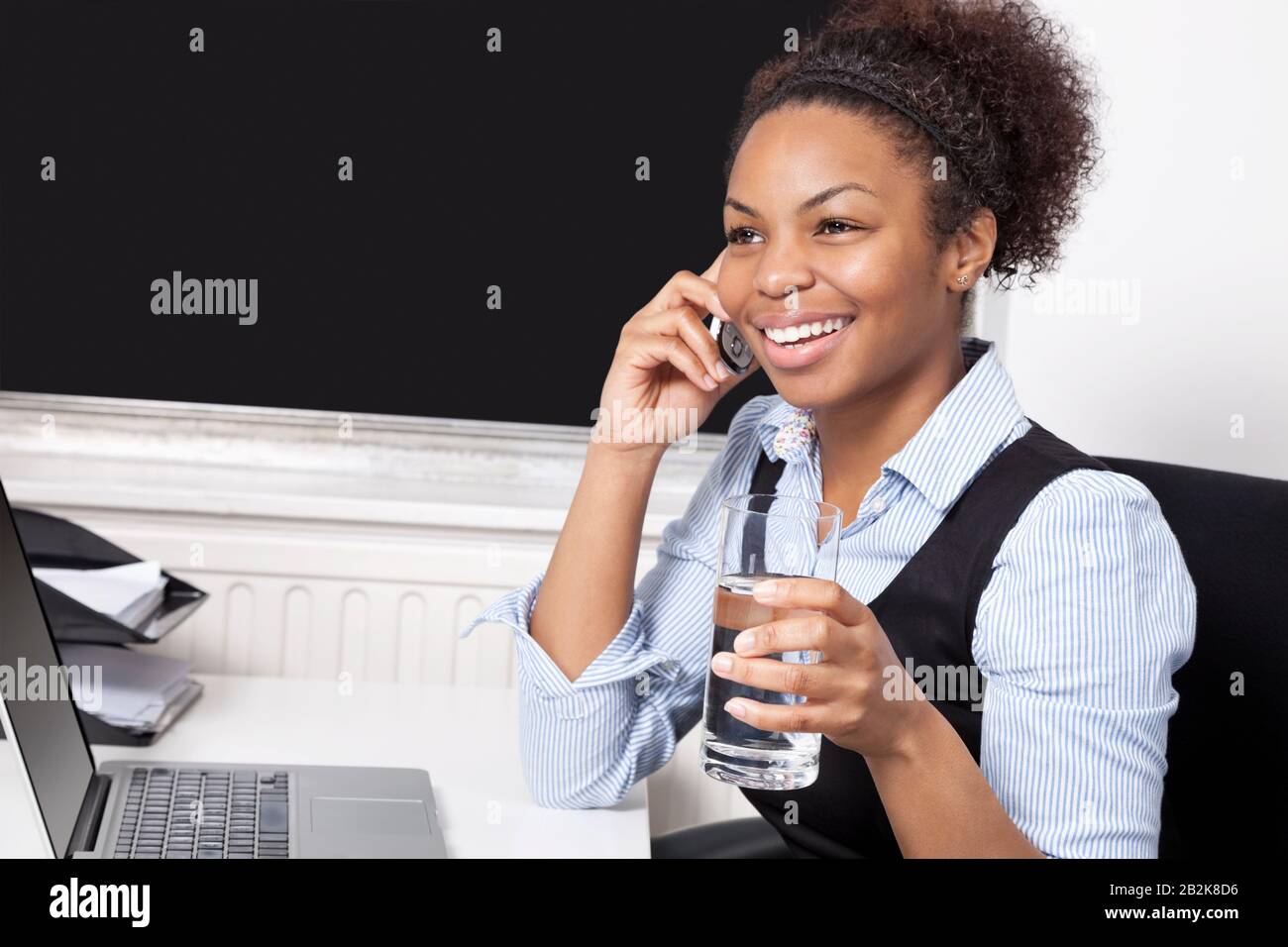 Donna d'affari felice che usa il telefono cellulare di fronte al portatile alla scrivania in ufficio Foto Stock