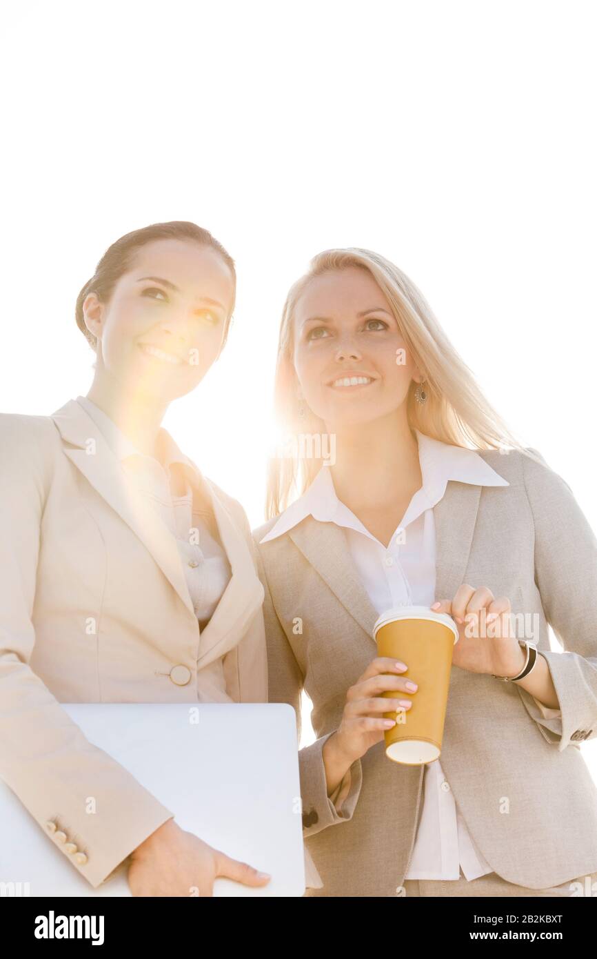 Giovani donne d'affari con una tazza usa e getta e un computer portatile che guarda lontano dal cielo Foto Stock