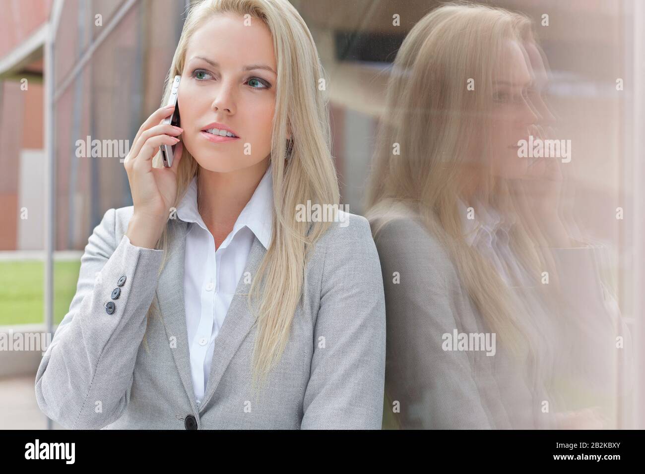 Bella bionda businesswoman conversare sul telefono cellulare mentre si guarda via da parete di vetro Foto Stock
