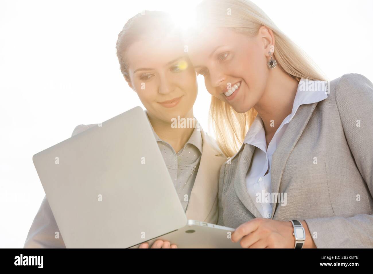 Buone giovani donne d'affari che usano il laptop contro il cielo Foto Stock